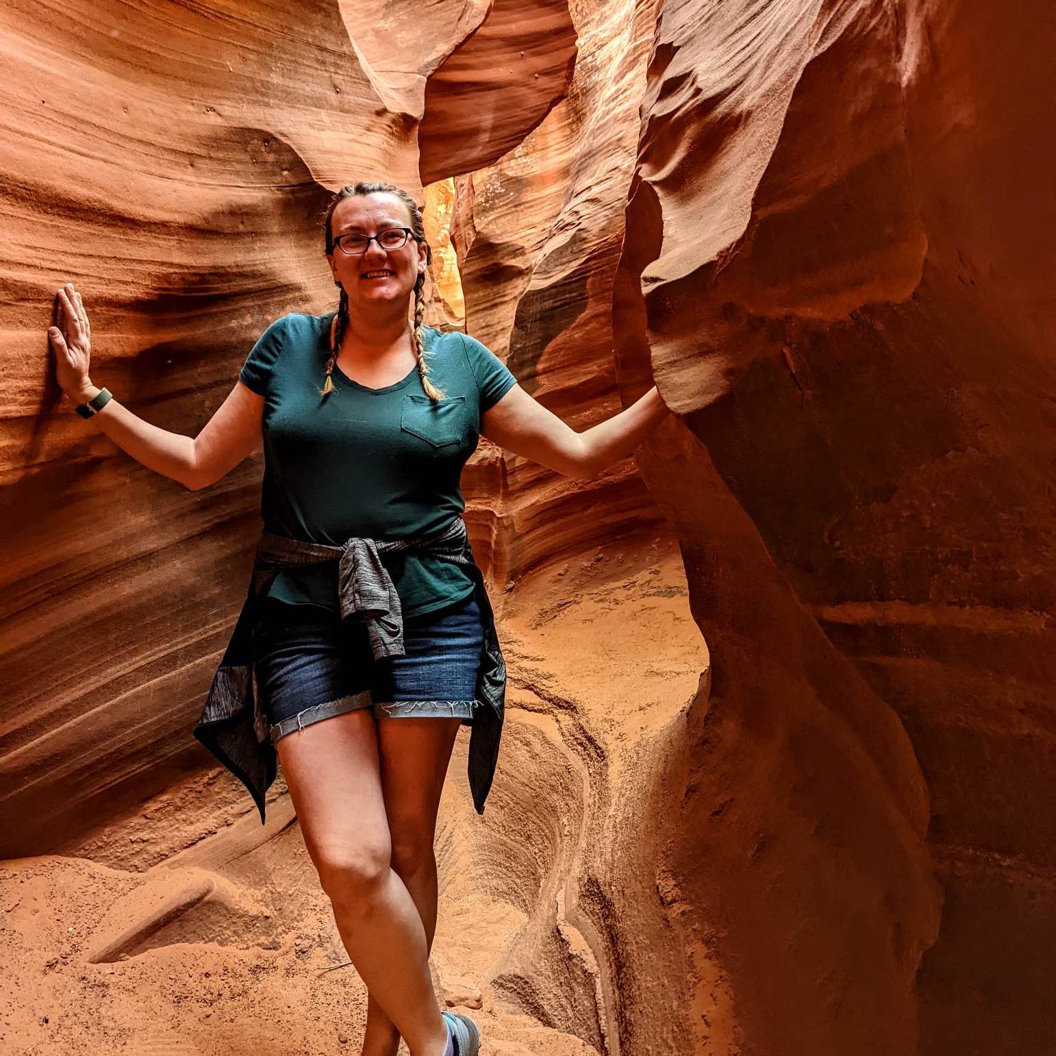 woman in hiking shoes, shorts, and t-shirt standing in a bright orage slot canyon