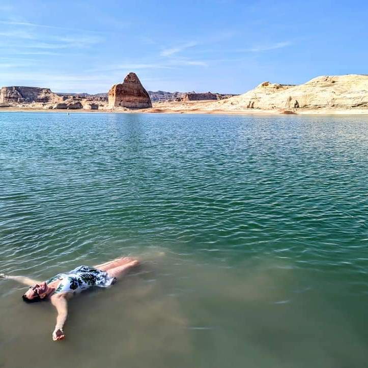 woman in a bathing suit floating in the water with desert rocks in the background