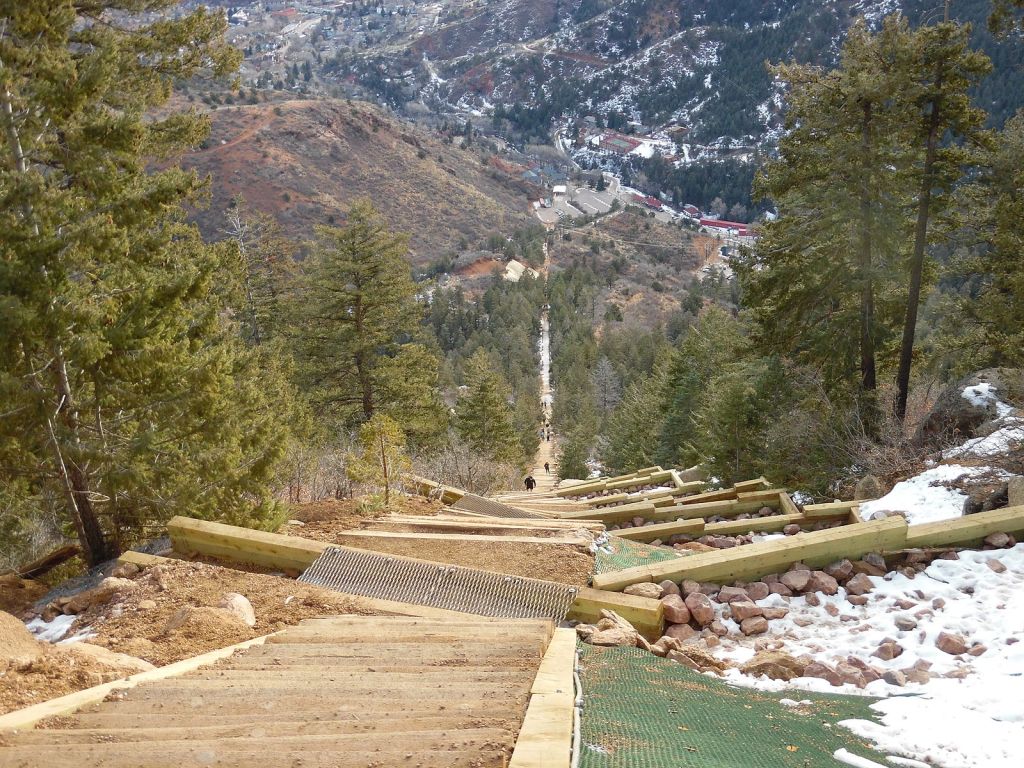 looking down a wooden staircase trail  up a steep mountainside with a city visible at the base