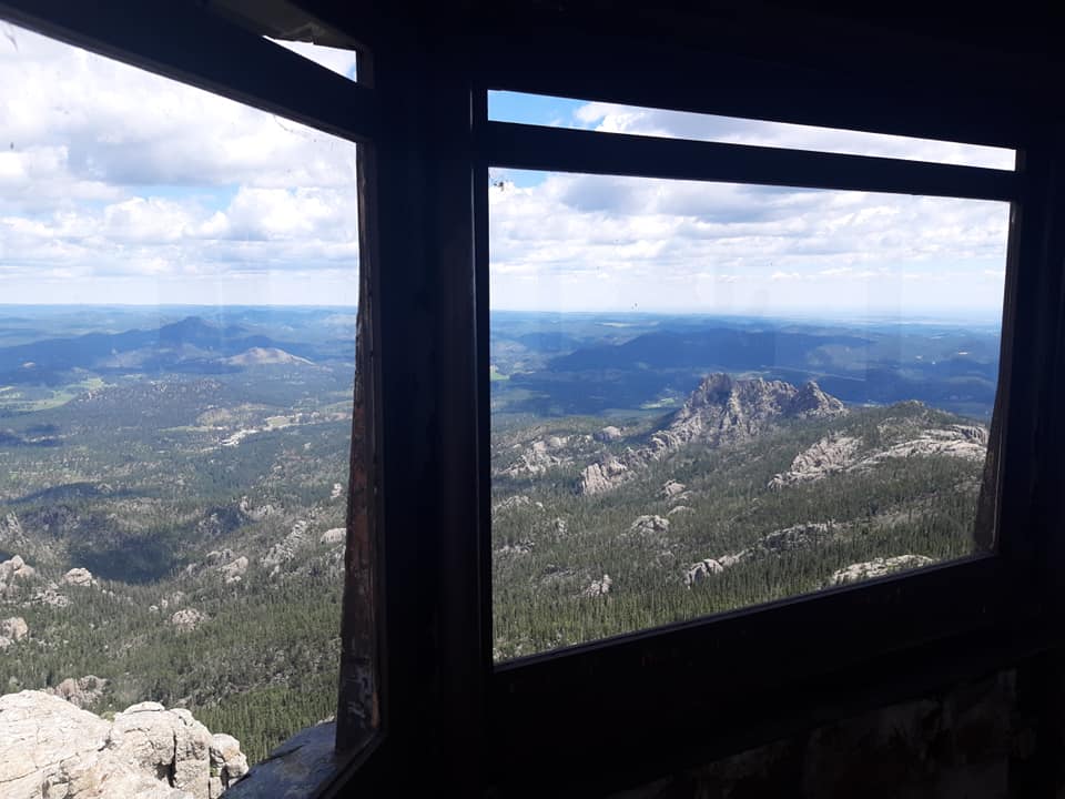 view out of the window of a fire tower overlooking rocky outcrops coming out of the forest below