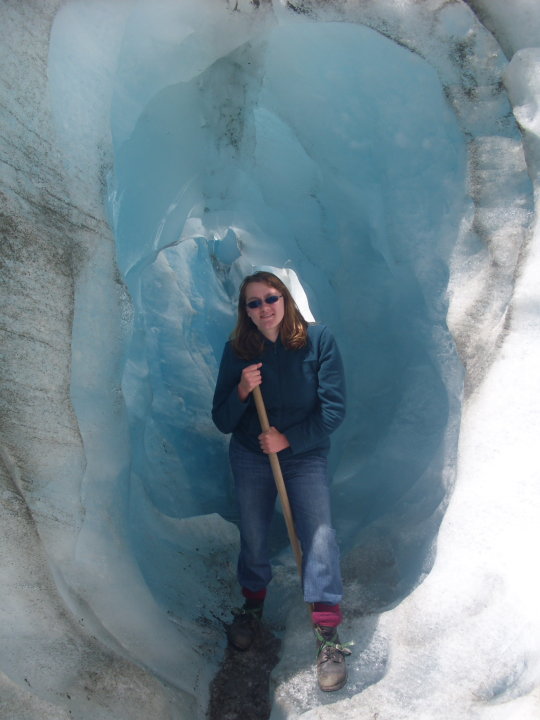 a woman in hiking gear stands inside of an ice cave on a glacier