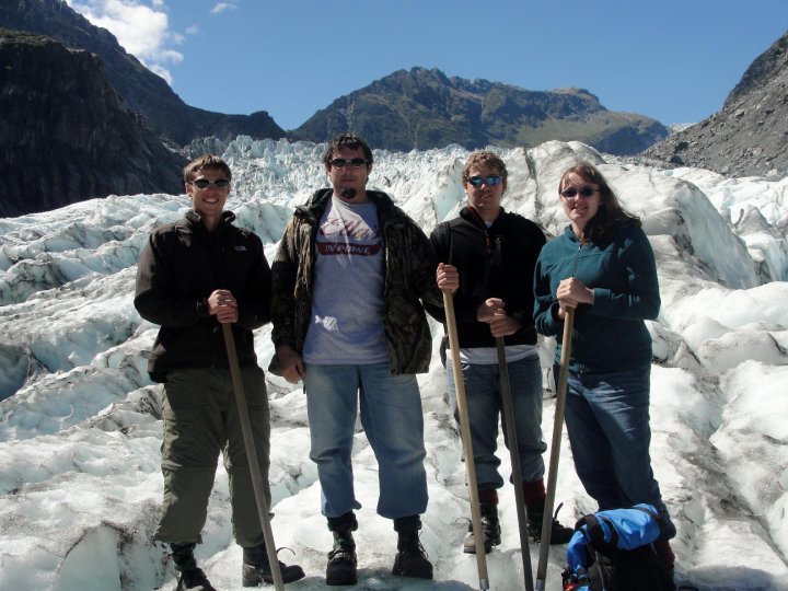 three men and one woman in hiking gear stand on top of a glacier