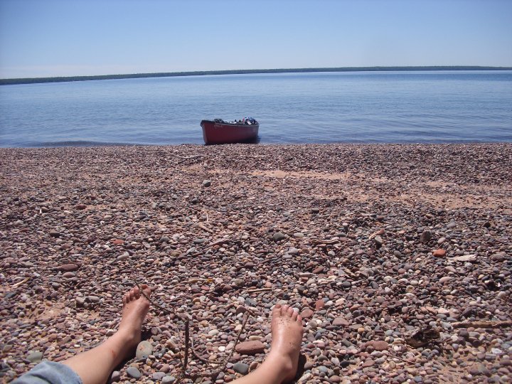 a cone sits out at the edge of the beach with bare hikers feet resting on the rocks