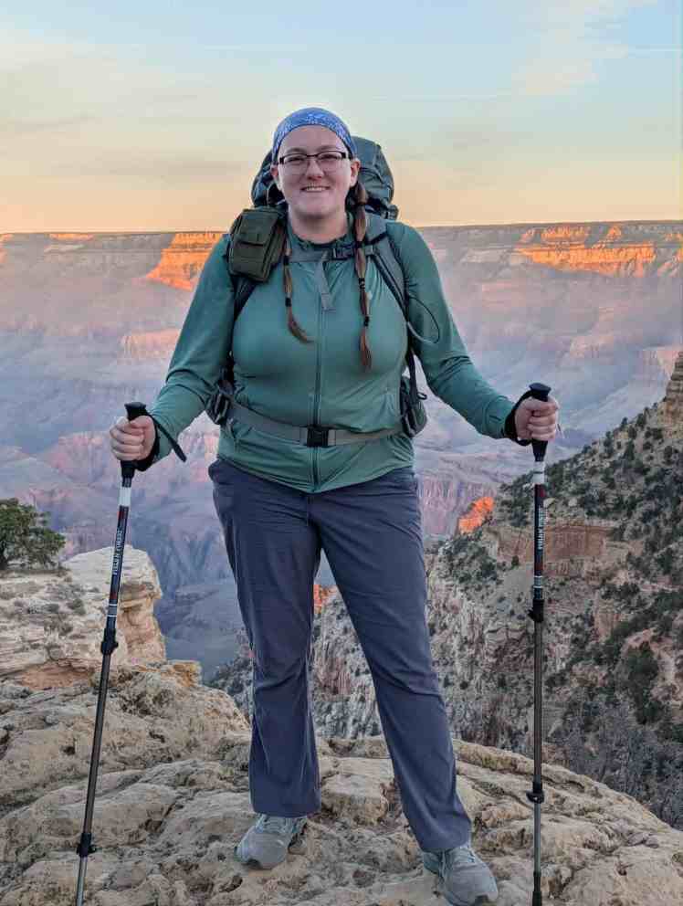 A female backpacker stands on the north rim of the Grand Canyon with her backpack and hiking poles
